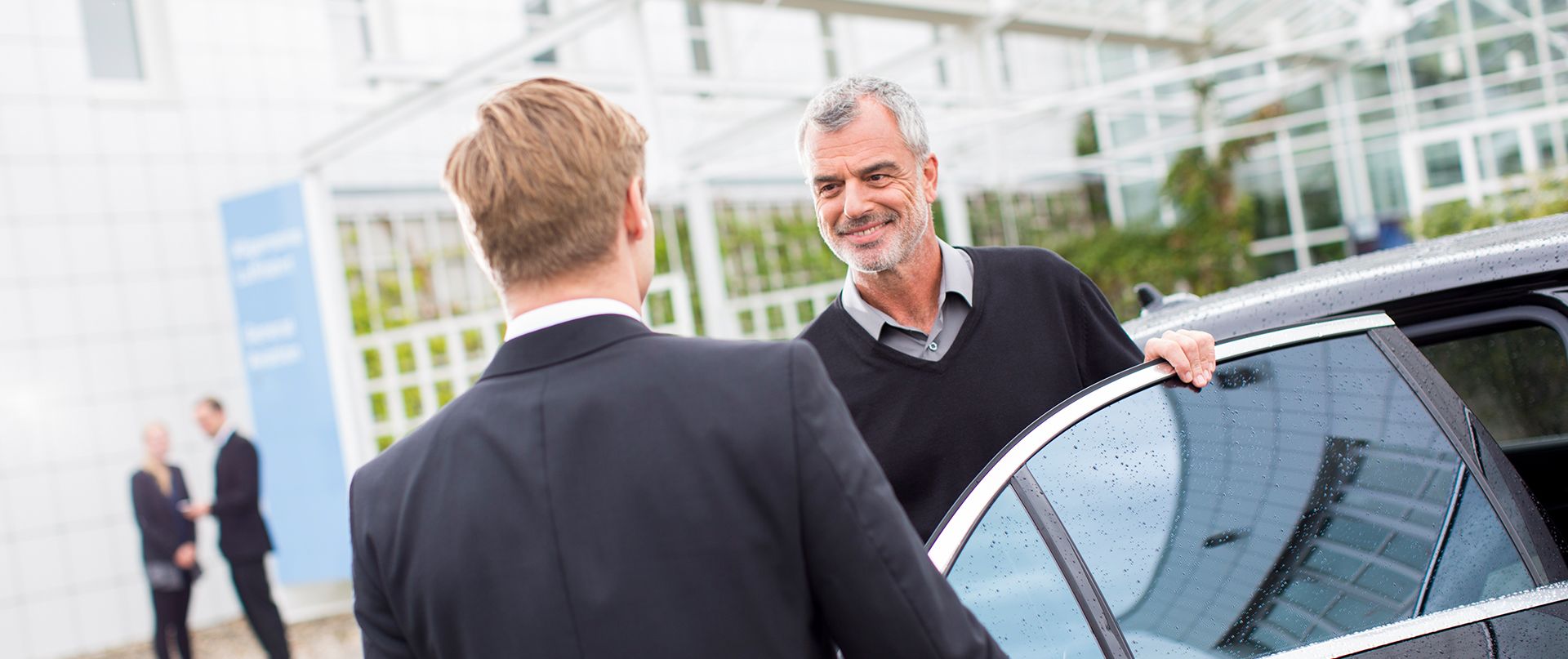 Ein Fahrgast steigt aus einer Limousine aus und spricht mit einem Chauffeur.