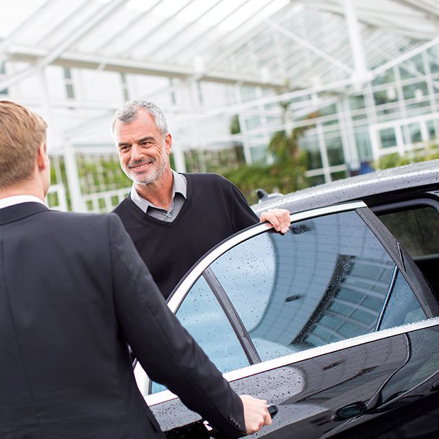 Ein Fahrgast steigt aus einer Limousine aus und spricht mit einem Chauffeur.